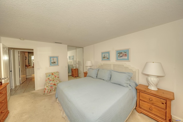 bedroom with connected bathroom, light colored carpet, and a textured ceiling