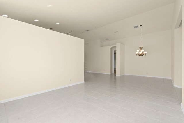 tiled spare room featuring vaulted ceiling and an inviting chandelier