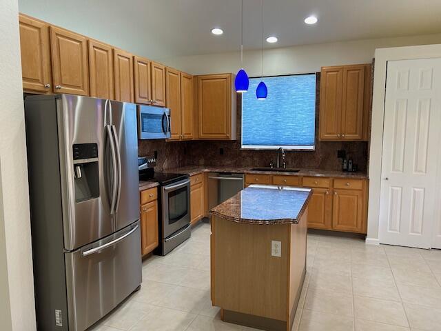 kitchen featuring a kitchen island, appliances with stainless steel finishes, dark stone countertops, decorative light fixtures, and a sink