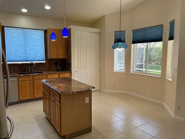 kitchen with brown cabinets, a center island, a sink, pendant lighting, and backsplash