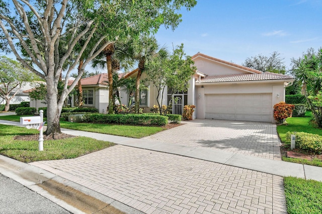 ranch-style house featuring an attached garage, a tiled roof, decorative driveway, stucco siding, and a front yard