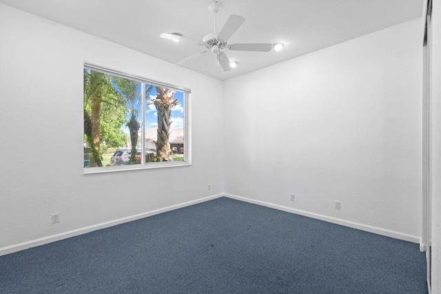 empty room featuring baseboards, dark carpet, and a ceiling fan