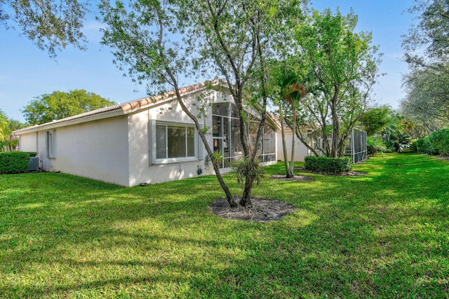 back of property with a yard, central air condition unit, a tile roof, and stucco siding