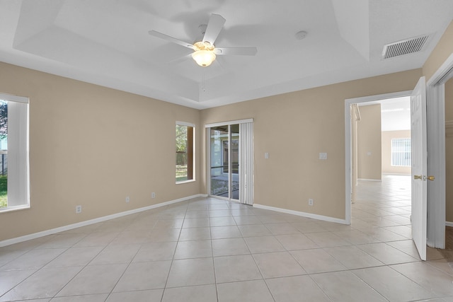 empty room with a tray ceiling, ceiling fan, and light tile patterned flooring