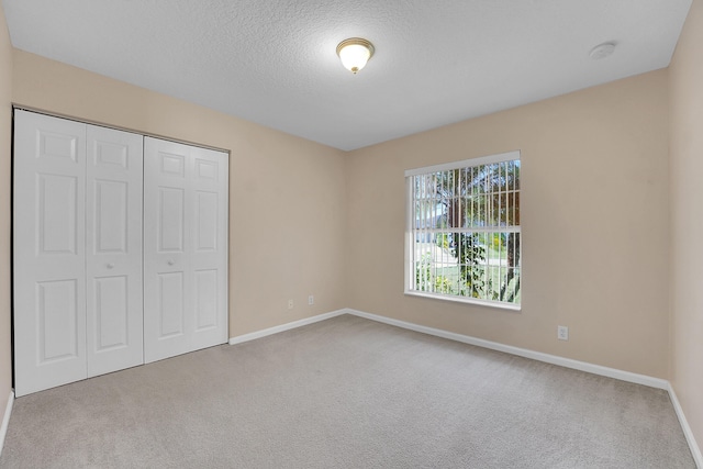 unfurnished bedroom featuring a textured ceiling, light carpet, and a closet