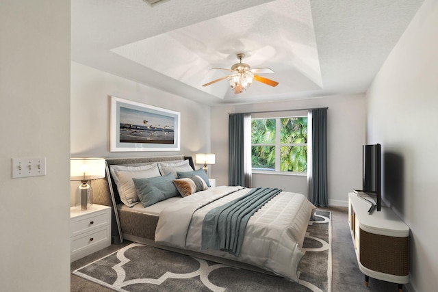 bedroom with ceiling fan, dark carpet, and a raised ceiling