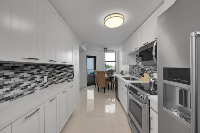 kitchen with backsplash, stainless steel appliances, sink, light tile patterned floors, and white cabinets