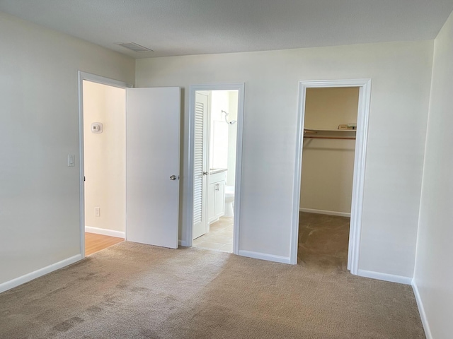 unfurnished bedroom with light carpet, a spacious closet, a closet, and ensuite bathroom