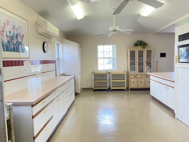 kitchen featuring tasteful backsplash, a textured ceiling, a wall unit AC, and white cabinets