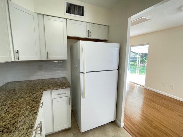 kitchen with light hardwood / wood-style flooring, backsplash, white cabinets, dark stone counters, and white fridge