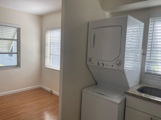 clothes washing area featuring a textured ceiling, sink, stacked washer / drying machine, and light hardwood / wood-style flooring