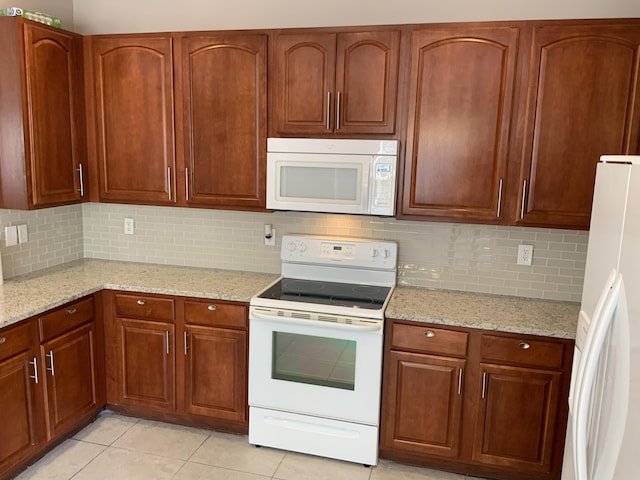 kitchen featuring light tile patterned floors, tasteful backsplash, white appliances, and light stone countertops