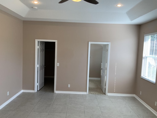 unfurnished bedroom featuring a spacious closet, baseboards, and a raised ceiling