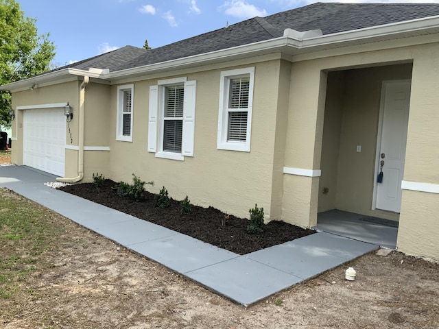 view of property exterior with an attached garage, stucco siding, and roof with shingles