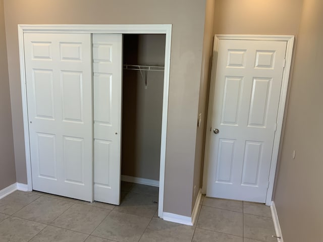 unfurnished bedroom featuring a closet, light tile patterned flooring, and baseboards