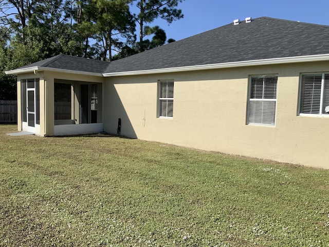 rear view of property with stucco siding, roof with shingles, a sunroom, and a yard