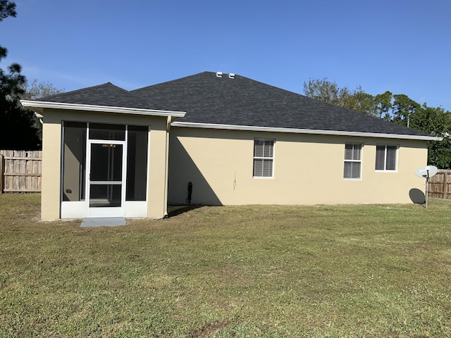 rear view of house with a yard, roof with shingles, fence, and stucco siding