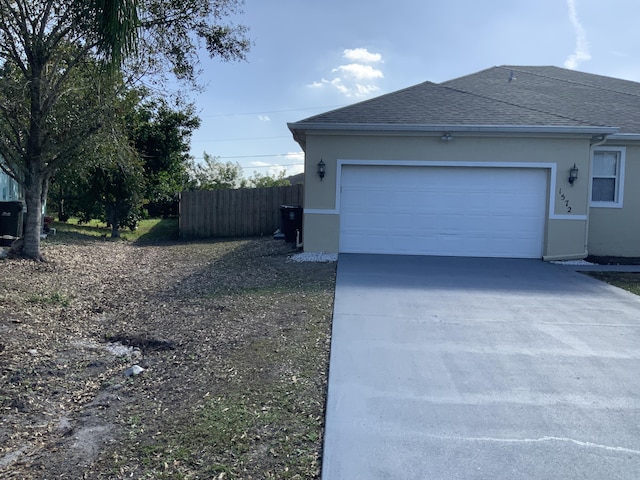 view of side of home with a shingled roof, driveway, an attached garage, and stucco siding