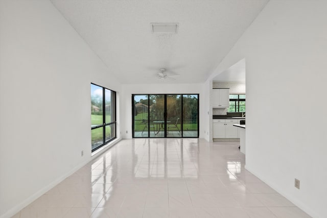 empty room with ceiling fan, light tile patterned floors, and a textured ceiling