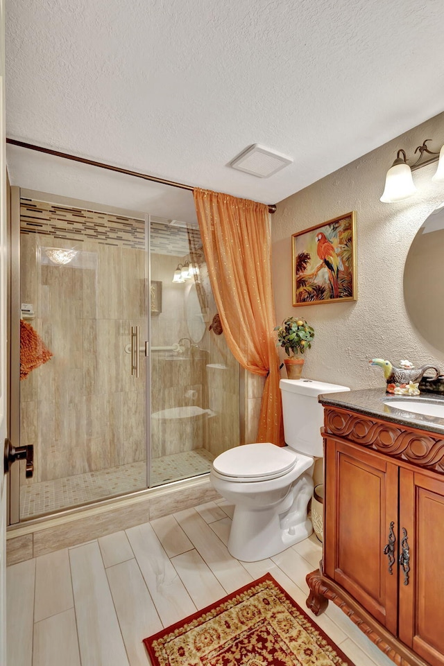 bathroom featuring tile patterned flooring, a textured ceiling, toilet, vanity, and a shower with shower door