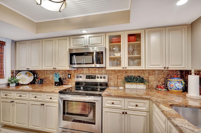 kitchen with a raised ceiling, stainless steel appliances, and cream cabinetry