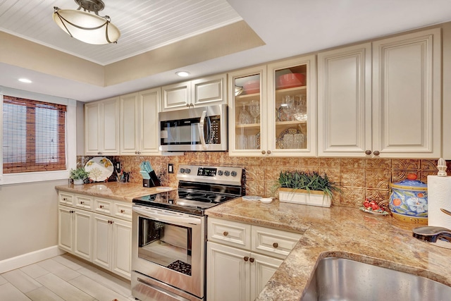 kitchen with appliances with stainless steel finishes, light stone counters, a tray ceiling, sink, and cream cabinetry