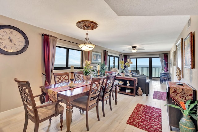 dining room featuring ceiling fan, a water view, light wood-type flooring, and a textured ceiling