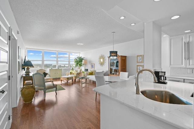 kitchen featuring light stone counters, sink, decorative light fixtures, a wall of windows, and white cabinetry