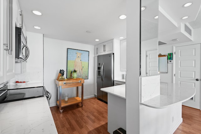 kitchen with hardwood / wood-style flooring, white cabinetry, light stone counters, kitchen peninsula, and stainless steel appliances