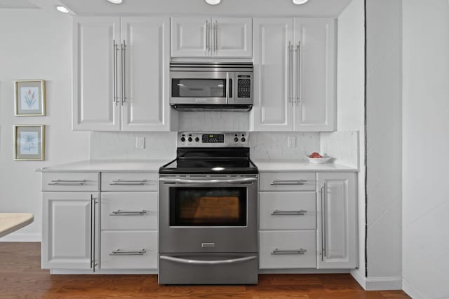 kitchen featuring decorative backsplash, appliances with stainless steel finishes, white cabinetry, and hardwood / wood-style floors