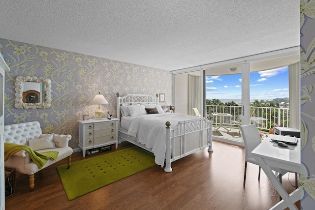 bedroom featuring access to exterior, wood-type flooring, a textured ceiling, and a wall of windows