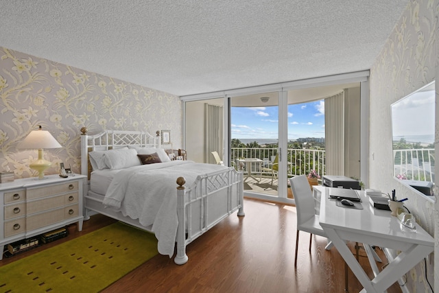 bedroom featuring hardwood / wood-style flooring, floor to ceiling windows, access to exterior, and a textured ceiling