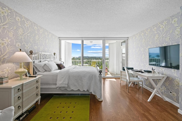 bedroom with access to exterior, dark hardwood / wood-style flooring, a textured ceiling, and a wall of windows