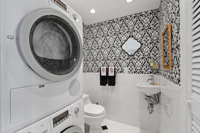 bathroom featuring tile patterned flooring, stacked washing maching and dryer, tile walls, and toilet