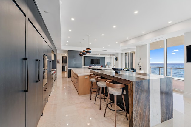 kitchen featuring a kitchen bar, floor to ceiling windows, decorative light fixtures, dark stone countertops, and a large island