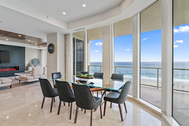 dining space with expansive windows, a fireplace, a water view, and a beach view