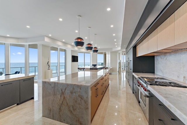 kitchen featuring range with two ovens, a water view, hanging light fixtures, light stone countertops, and a large island