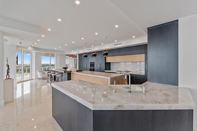 kitchen with sink, decorative light fixtures, light stone countertops, tasteful backsplash, and a large island