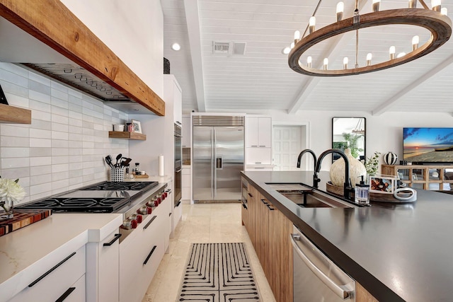 kitchen with beamed ceiling, appliances with stainless steel finishes, white cabinetry, and sink