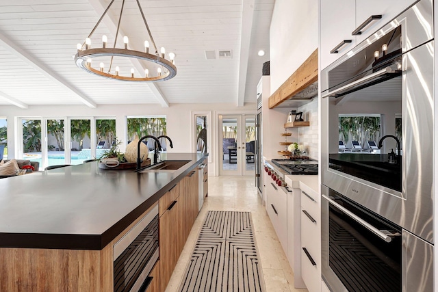 kitchen with appliances with stainless steel finishes, tasteful backsplash, a kitchen island with sink, beam ceiling, and white cabinets