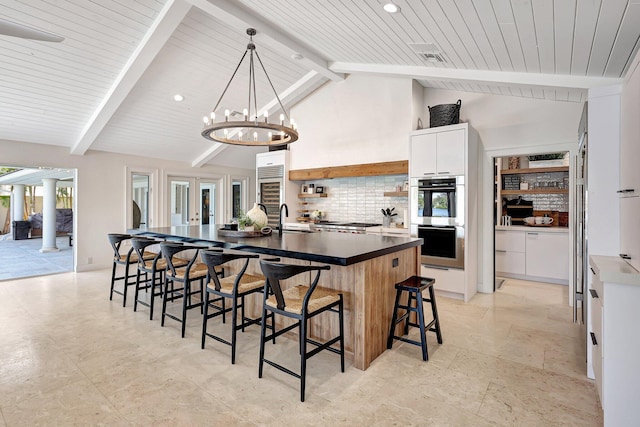 kitchen featuring sink, vaulted ceiling with beams, a chandelier, a kitchen island with sink, and white cabinets