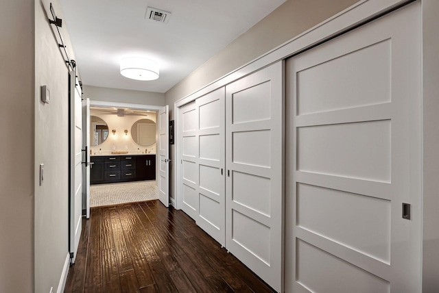 corridor with a barn door and dark hardwood / wood-style flooring