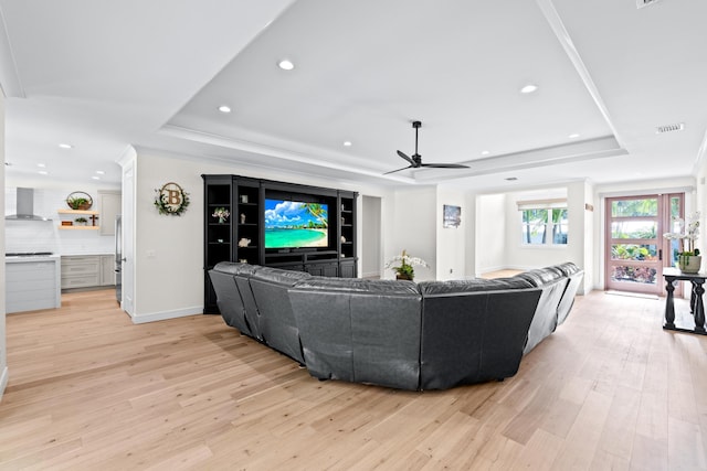 living room with light hardwood / wood-style floors, a raised ceiling, ceiling fan, and crown molding