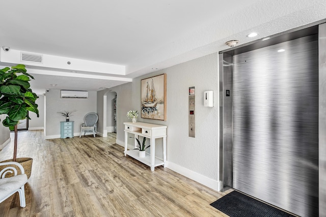 interior space with elevator, a wall mounted air conditioner, and light wood-type flooring