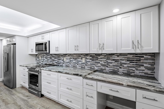 kitchen featuring tasteful backsplash, stainless steel appliances, dark stone countertops, light hardwood / wood-style floors, and white cabinetry