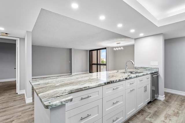 kitchen with light hardwood / wood-style floors, light stone counters, white cabinetry, and sink