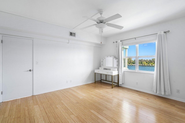 unfurnished room featuring a water view, ceiling fan, and light wood-type flooring