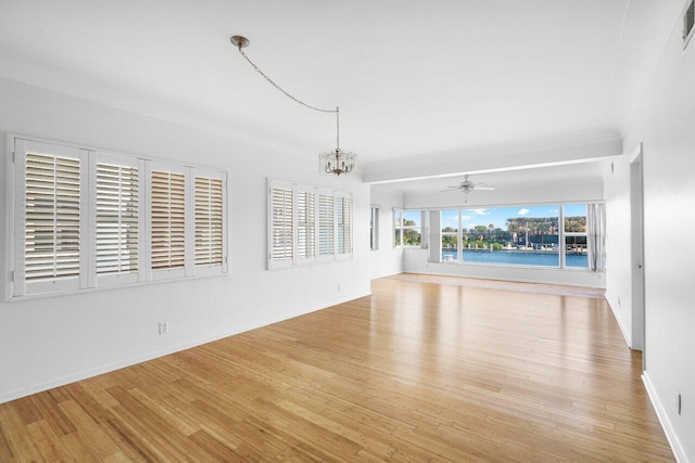 unfurnished living room featuring a water view, ceiling fan with notable chandelier, and light hardwood / wood-style flooring