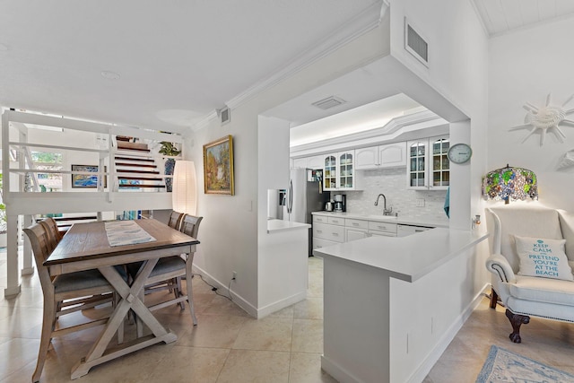 kitchen featuring white cabinetry, sink, kitchen peninsula, light tile patterned floors, and ornamental molding