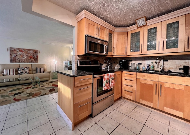 kitchen with sink, kitchen peninsula, dark stone counters, light tile patterned floors, and appliances with stainless steel finishes